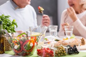 older man sitting at a table full of varied and colorful food, fruits, and vegetables savoring the importance of a good culinary experience
