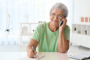 senior woman sitting at kitchen table talking on the phone and learning about the average cost of senior living in texas