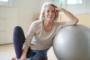 healthy, fit older woman sitting on floor leaning against exercise ball demonstrating the seven different elements of senior wellness