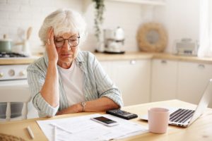 female senior sitting at table staring at bills and calculator in confusing displaying some of the 10 early signs of dementia in seniors