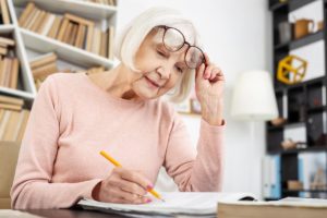 senior woman working a crossword while positioning a pair of reading glasses demonstrating common causes of vision loss in seniors