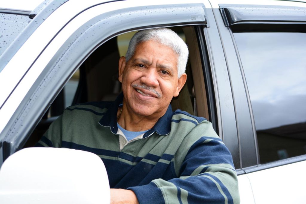 older male driver looking out car window and smiling while onlookers wonder is it safe for your senior to still be driving