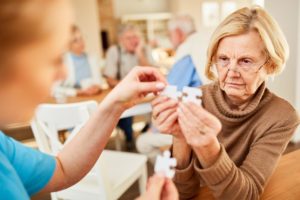 older woman attempting to assemble puzzle pieces while caregiver wonders what are the physical symptoms of dementia