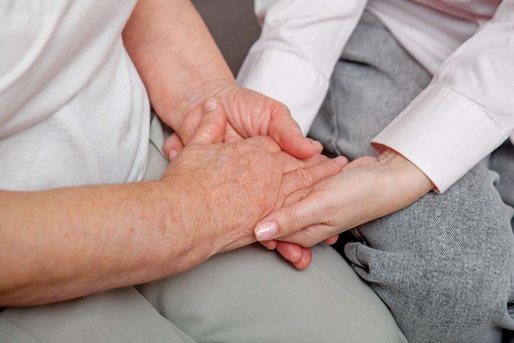 close up of a younger person holding an older person's hand and employing one of 10 tips for caring for a loved one with dementia