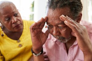 a senior grips their head as a caregiver looks on wondering how to manage these difficult dementia behaviors