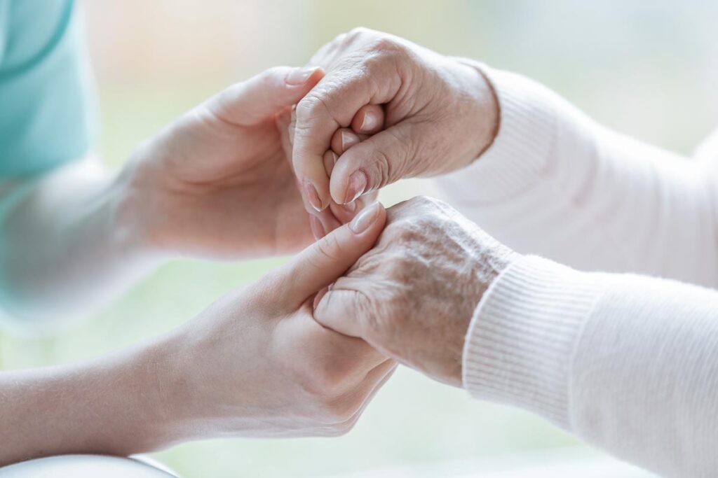 an adult child holds the hands of a senior as they prepare for memory care