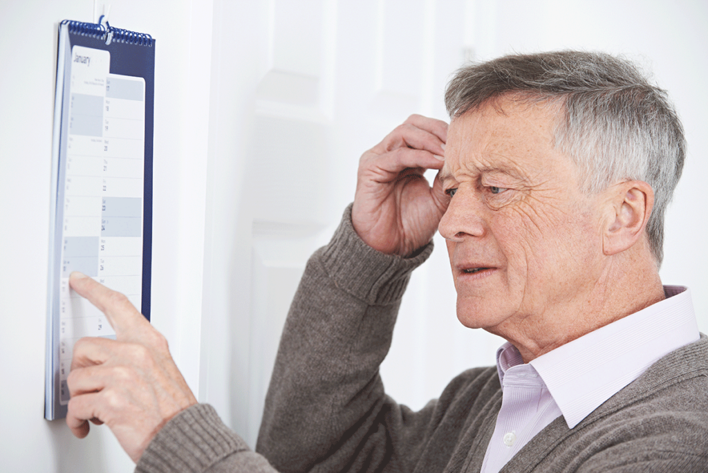 a senior looks at a calendar and holds their head showing early signs of dementia