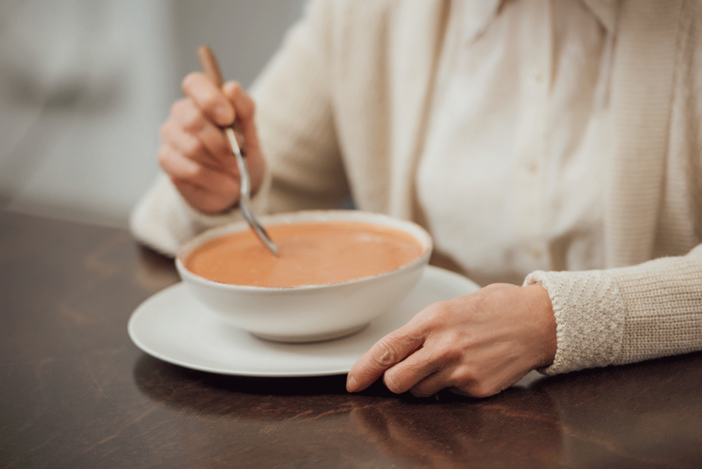 a senior woman eats a bowl of tomato soup