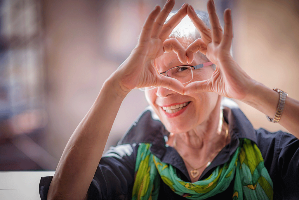 a senior woman makes a heart with her hands