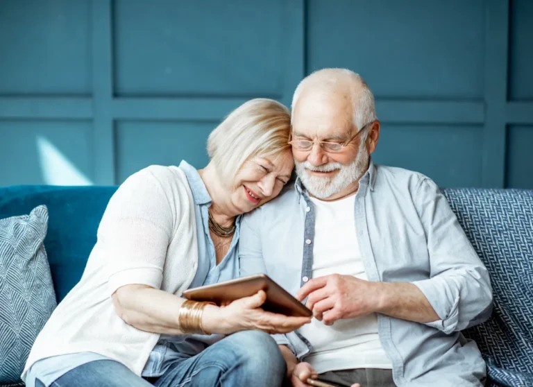 Smiling older couple sitting on a couch, looking at a tablet together and enjoying each other's company.
